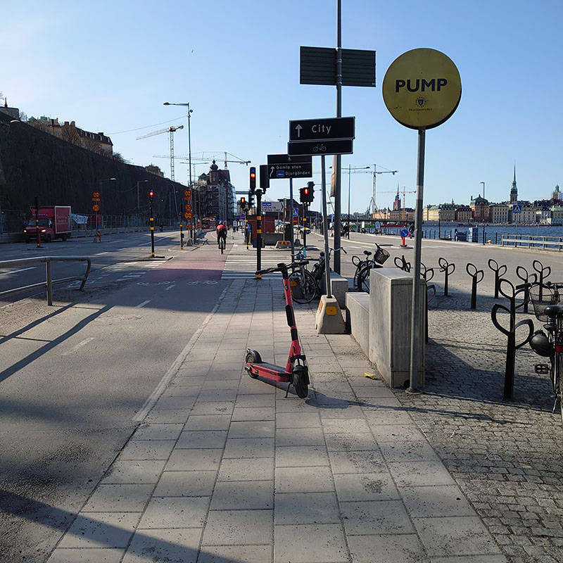 Bilden visar en gångbana med stökig temporär skyltuppsättning, och en elscooter ställd mitt i gångvägen.